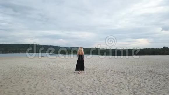 沙滩上穿着黑色裙子的金发女人视频的预览图