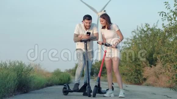 这个女孩和她的男朋友骑电动滑板车在风电场的背景下自拍视频的预览图