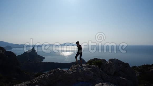 勇敢的年轻女孩走在悬崖上欣赏美丽的海景和最明亮的太阳前面视频的预览图