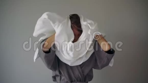 穿着灰色浴衣的年轻快乐的女人用毛巾擦干头发视频的预览图