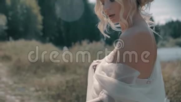 穿着白色裙子的金发女孩坐在湖边视频的预览图