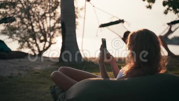 年轻的白种人女人躺在一个大枕头上用智能手机视频的预览图