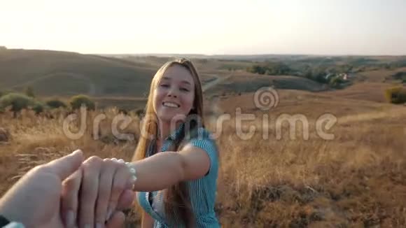 美丽甜美的女孩牵着男友手带着他沿着田野在夕阳的映衬下视频的预览图