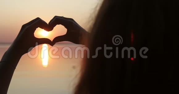 抬起头和手一个女孩在日落时用手做心脏的剪影视频的预览图
