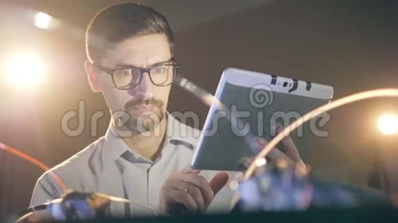 一个戴眼镜的人正在操作平板电脑同时观察一个3D打印机视频的预览图