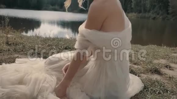穿着白色裙子的金发女孩坐在靠近湖边视频的预览图
