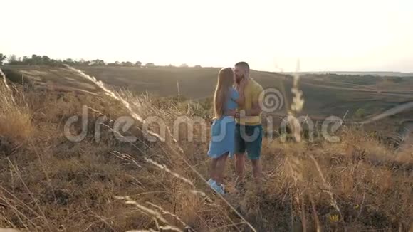 在一片荒芜的田野里一对可爱的年轻夫妇在一片耀眼的阳光下亲吻和拥抱A视频的预览图