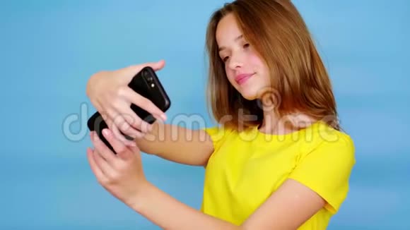 穿黄色T恤的快乐少女在智能手机上自拍或视频并微笑视频的预览图