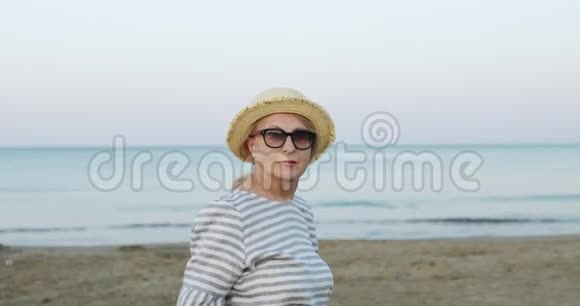 清晨日出时戴着草帽的欢快的老妇人在海边散步视频的预览图