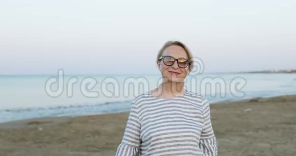 阳光明媚的老年妇女清晨在海边沙滩上日出视频的预览图