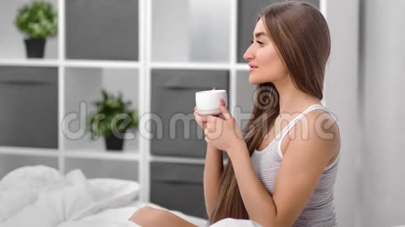 微笑的家庭妇女在床上喝茶享受平静的早晨中型摄影机视频的预览图