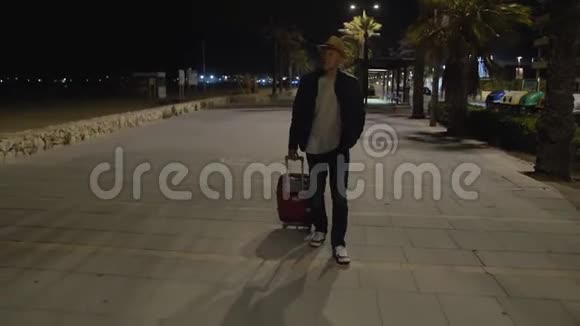 带帽子和手提箱的旅行者深夜在街上散步视频的预览图