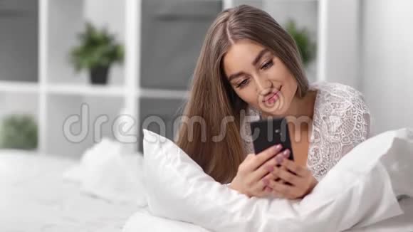 肖像美丽的女性穿着睡衣使用智能手机躺在床上近距离拍摄4k红色相机视频的预览图