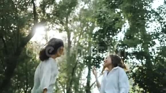 两个快乐的漂亮女朋友在草地上跳舞和跳跃在一个温暖的阳光明媚的日子里摆姿势有趣的照片视频的预览图