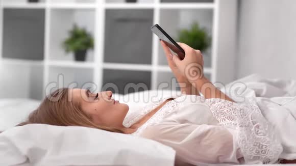放松的女人躺在舒适的床上用智能手机聊天中型近距离拍摄4k红色相机视频的预览图