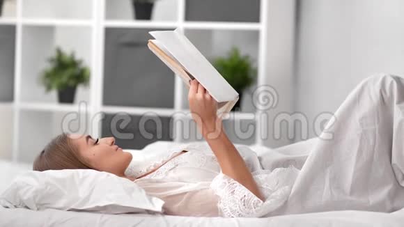 平静放松的女人躺在床上穿着内衣看书中型摄影机视频的预览图