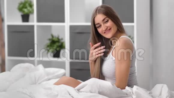 迷人的家庭女孩微笑着坐在舒适的卧室的床上中型摄影机视频的预览图