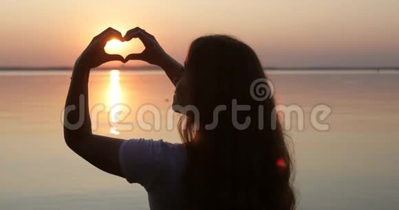 一个女孩在日落时用手做心脏的剪影视频的预览图