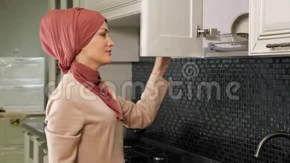 戴头巾的女人打开厨房橱柜拿干净盘子视频的预览图