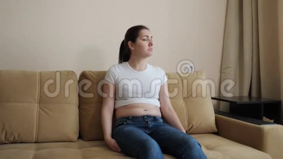 年轻的女人坐在沙发上伤心脂肪沉积在腹部视频的预览图