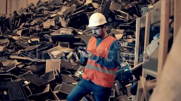 一个拿着智能手机的垃圾场工人正站在一堆垃圾附近视频的预览图