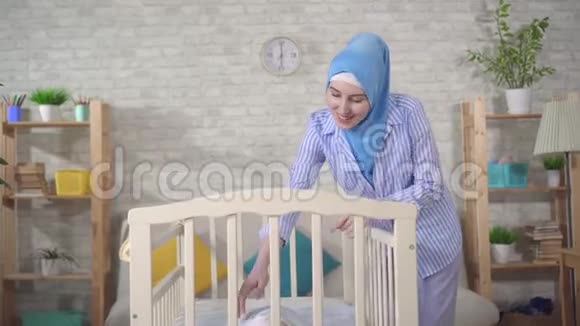 幸福的年轻母亲在婴儿的婴儿床上戴着头巾视频的预览图