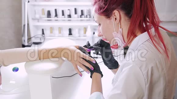 美容院的女美甲师在顾客的指甲上涂上紫色的凝胶抛光剂视频的预览图