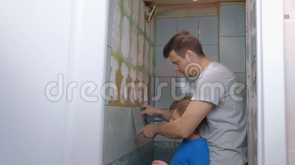 爸爸和儿子在家里一起做装修把厕所里的墙上的瓷砖去掉视频的预览图