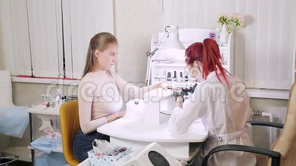 美容院的女美甲师给顾客的指甲涂上紫色的凝胶油那女孩用干指甲的方法视频的预览图