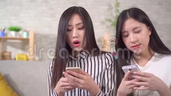 客厅里的沙发上有两个带着智能手机的快乐的年轻亚洲女孩视频的预览图