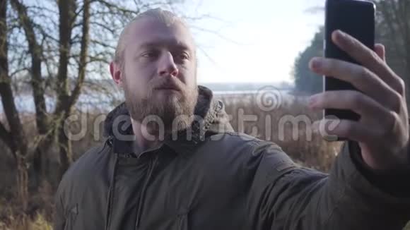 一个自信的白人男人留着胡子和马尾辫站在秋天的森林里自拍男性游客视频的预览图