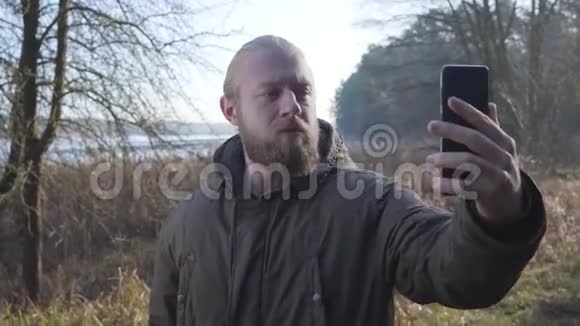 快乐白种人站在秋林湖前自拍的肖像他的男性游客视频的预览图