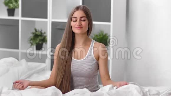 微笑放松的女性练习瑜伽姿势坐在床上享受早晨4k龙红相机视频的预览图