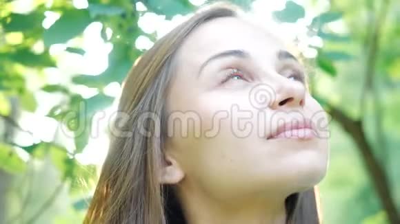一个漂亮的年轻女人的脸在一个舒适的城市公园里在树木和阳光的背景下近距离观看可爱的模特女孩视频的预览图