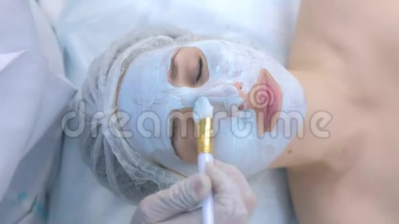 美容师使用刷子顶部视图在女性面部应用面部保湿面膜视频的预览图