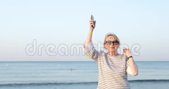 戴墨镜的金发老妇人正在沙滩上跳舞视频的预览图