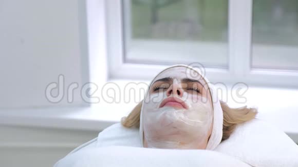 女性躺在水疗沙龙的肖像脸上戴着白色面具底部景色视频的预览图
