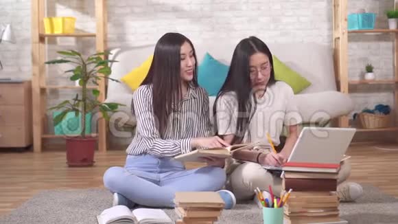 两个快乐的年轻亚洲学生坐在地板上手里拿着课本慢悠悠视频的预览图