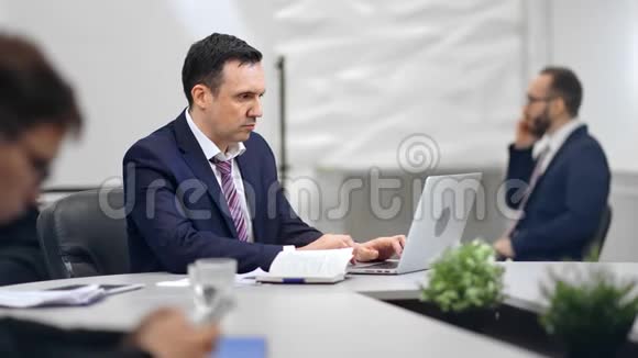 忙碌的男老板工作在笔记本电脑上周围是现代工作场所的同事视频的预览图