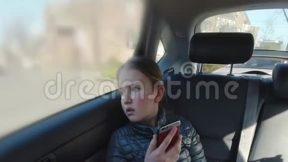 无聊的女孩坐在汽车后座看着智能手机2视频的预览图