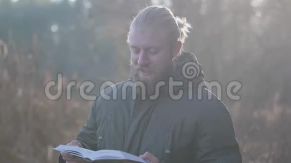 英俊的白种人肖像灰色的眼睛和胡须站在秋天的森林和阅读快乐的游客视频的预览图