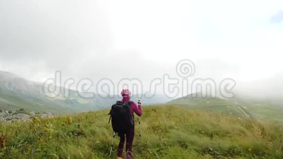 北欧旅游妇女手拿棍子和一个大背包在高加索山脉的一座高山上的草地上行走视频的预览图