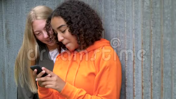 漂亮的金发女孩和混血的青少年女性在社交媒体上的智能手机上自拍视频的预览图