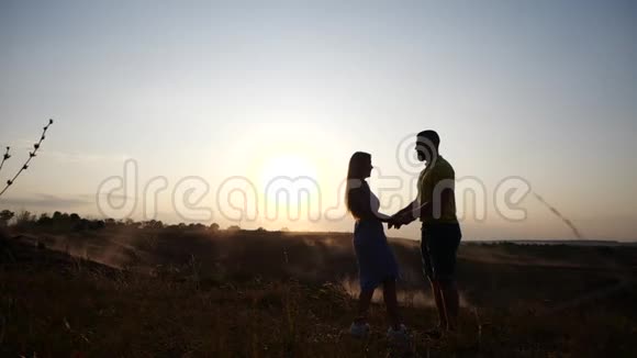 快乐的年轻人和女孩在夕阳的背景下缓慢地亲吻和拥抱在田野上可爱的一对视频的预览图