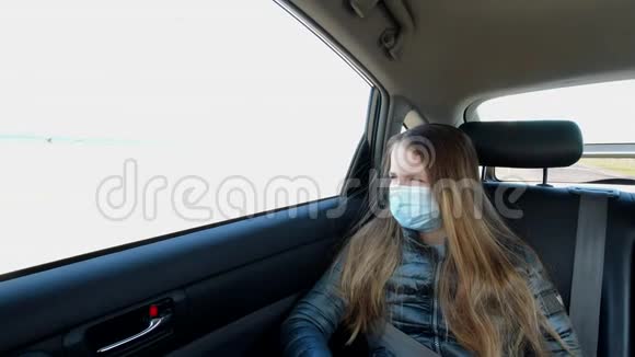 戴口罩的无聊病女孩坐在汽车后座看着车窗视频的预览图