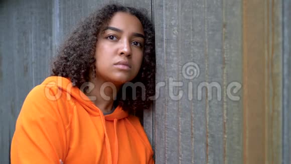 在城市环境中穿着橙色连帽衫的非洲裔美国少女少女看起来悲伤或体贴视频的预览图