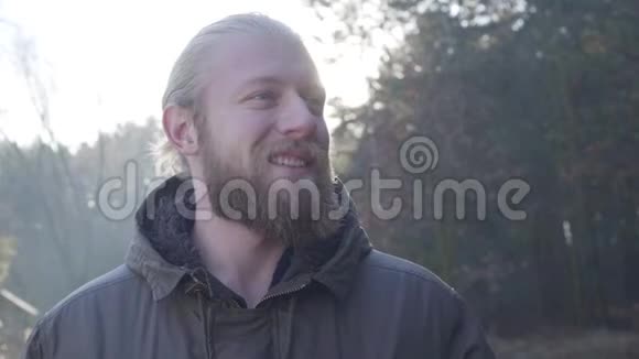 一个英俊的白种人灰色的眼睛站在秋天森林的阳光下微笑的游客享受他的视频的预览图