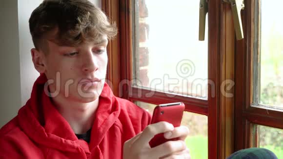 青少年男青少年穿红色帽衫使用手机发短信或社交媒体视频的预览图