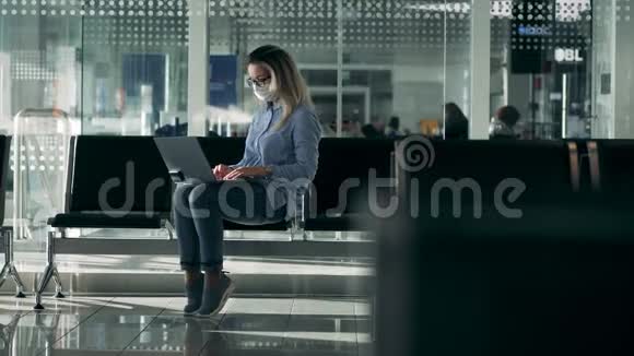 冠状病毒流行大流行的概念戴着医用口罩的可爱女人正在大厅里的笔记本电脑上工作视频的预览图