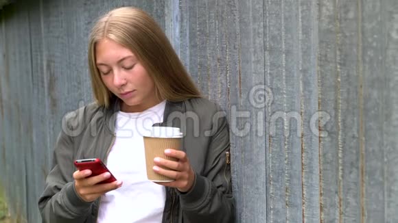 年轻的金发少女使用智能手机或手机社交媒体喝外卖咖啡视频的预览图